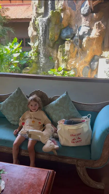 child sitting on couch wearing an oversized t-shirt next to an oversized tote bag