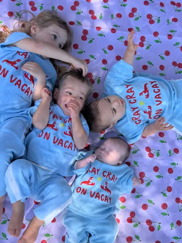 Four children in matching blue pants and top with red text on a cherry-patterned blanket.
