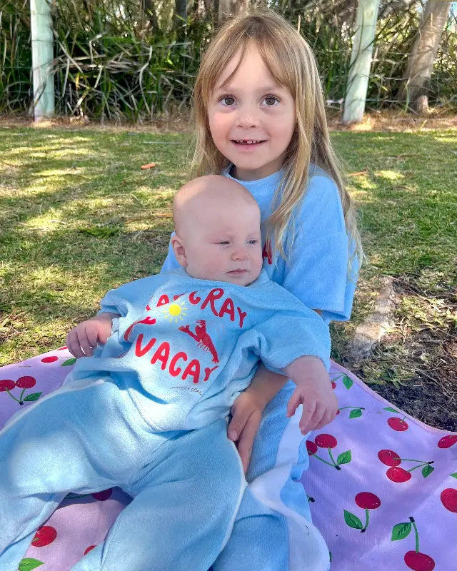 Two children in matching blue terry cloth pants set sitting on a blanket outdoors.