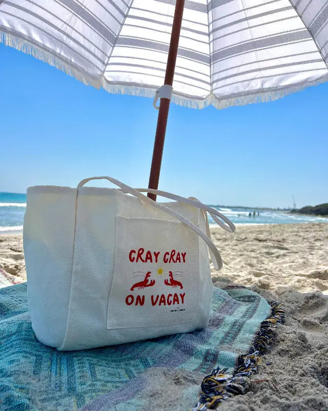 Beige beach tote bag with colourful logo on a beach holiday under an umbrella