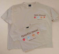 Two beige-colored t-shirts with snack-themed graphics and text on a beige background