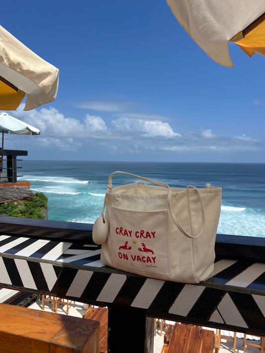 Beige tote bag with 'CRAY CRAY ON VACAY' text on a balcony with ocean view
