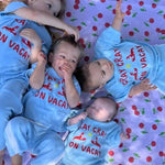 Four children in matching blue pants and top with red text on a cherry-patterned blanket.