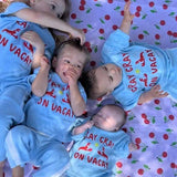 Four children in matching blue pants and top with red text on a cherry-patterned blanket.