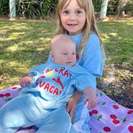 Two children in matching blue terry cloth pants set sitting on a blanket outdoors.