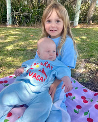 Two children in matching blue terry cloth pants set sitting on a blanket outdoors.