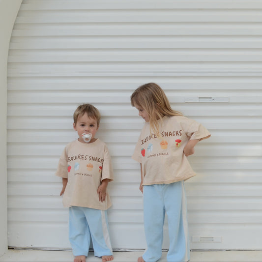 Two children wearing matching beige shirts with text standing in front of a white garage door.