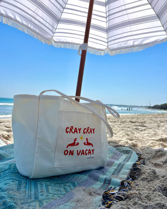 Beige beach tote bag with colourful logo on a beach holiday under an umbrella 