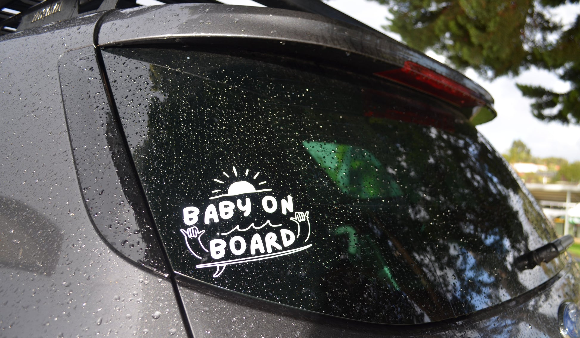 Car window with 'Baby on Board' sticker and raindrops