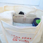 Canvas Beige tote bag with 'Cray Cray on Vacay' text, containing folded clothes and a blue container.