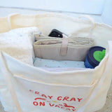 Canvas Beige tote bag with 'Cray Cray on Vacay' text, containing folded clothes and a blue container.