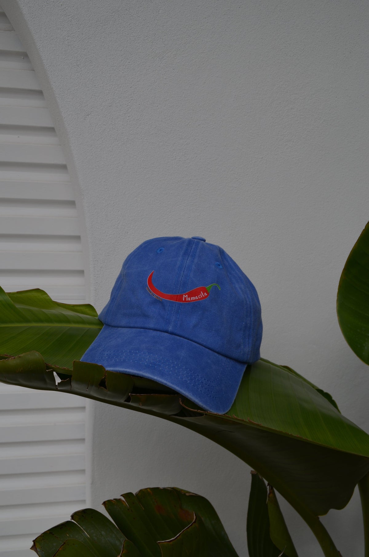Blue cap with a red chili pepper mamacita logo on from compass and cradle