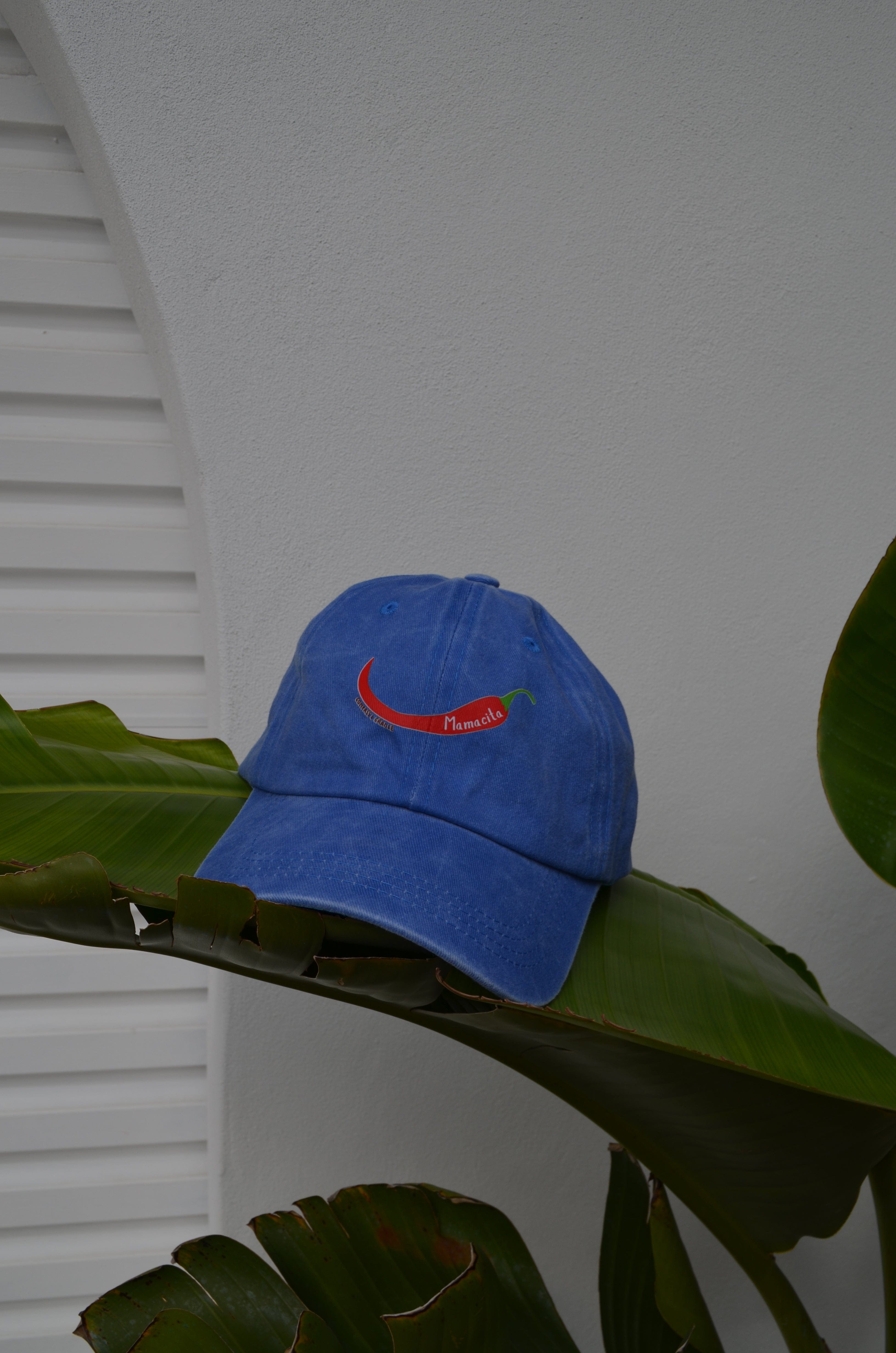 Blue cap with a red chili pepper mamacita logo on from compass and cradle