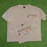 Two beige-colored t-shirts with snack-themed graphics and text on a beige background